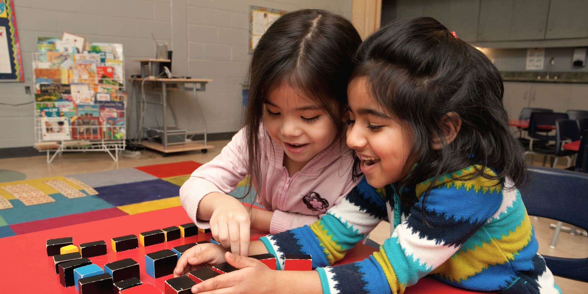 Two preschoolers laughing together while working with Montessori knobless cylinders