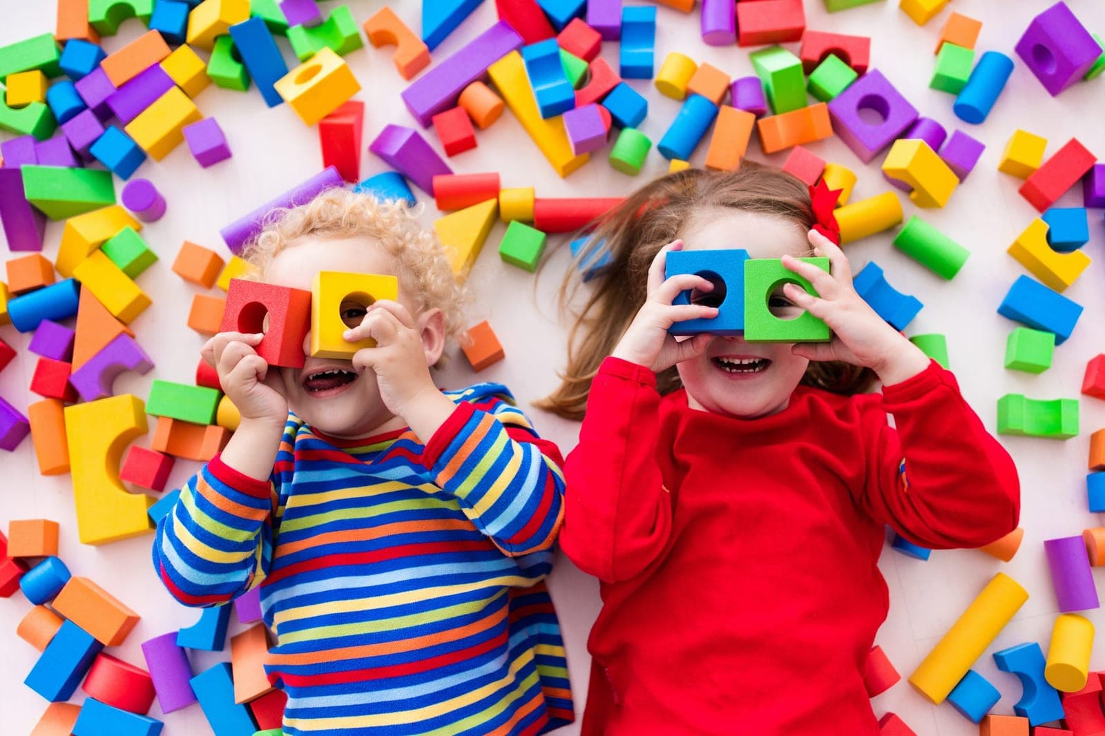 Two laughing children peering through colourful toy blocks