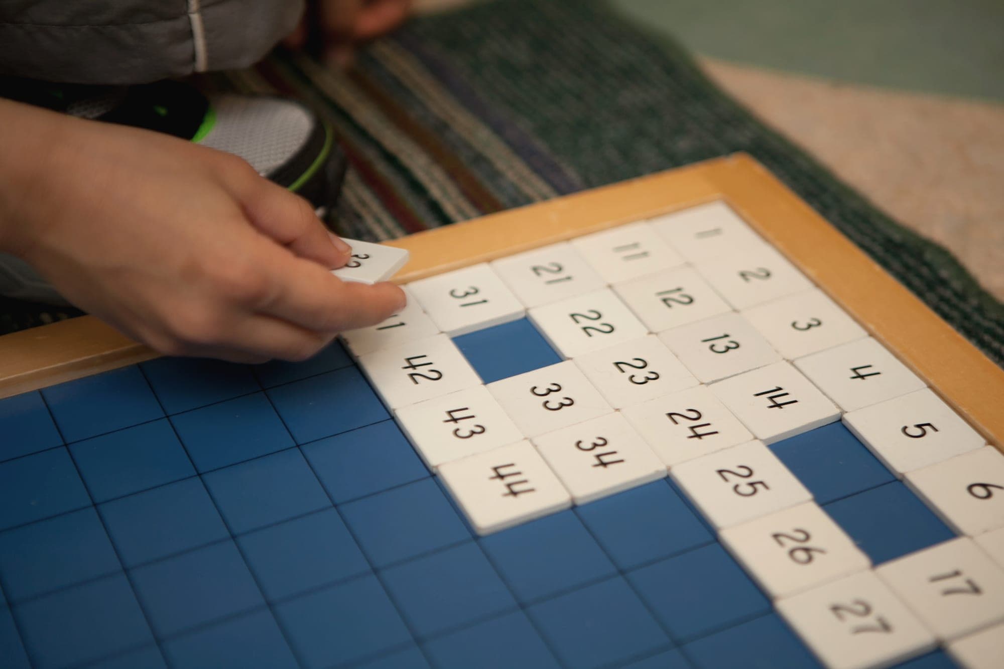 A child placing number tiles on a Montessori hundred board