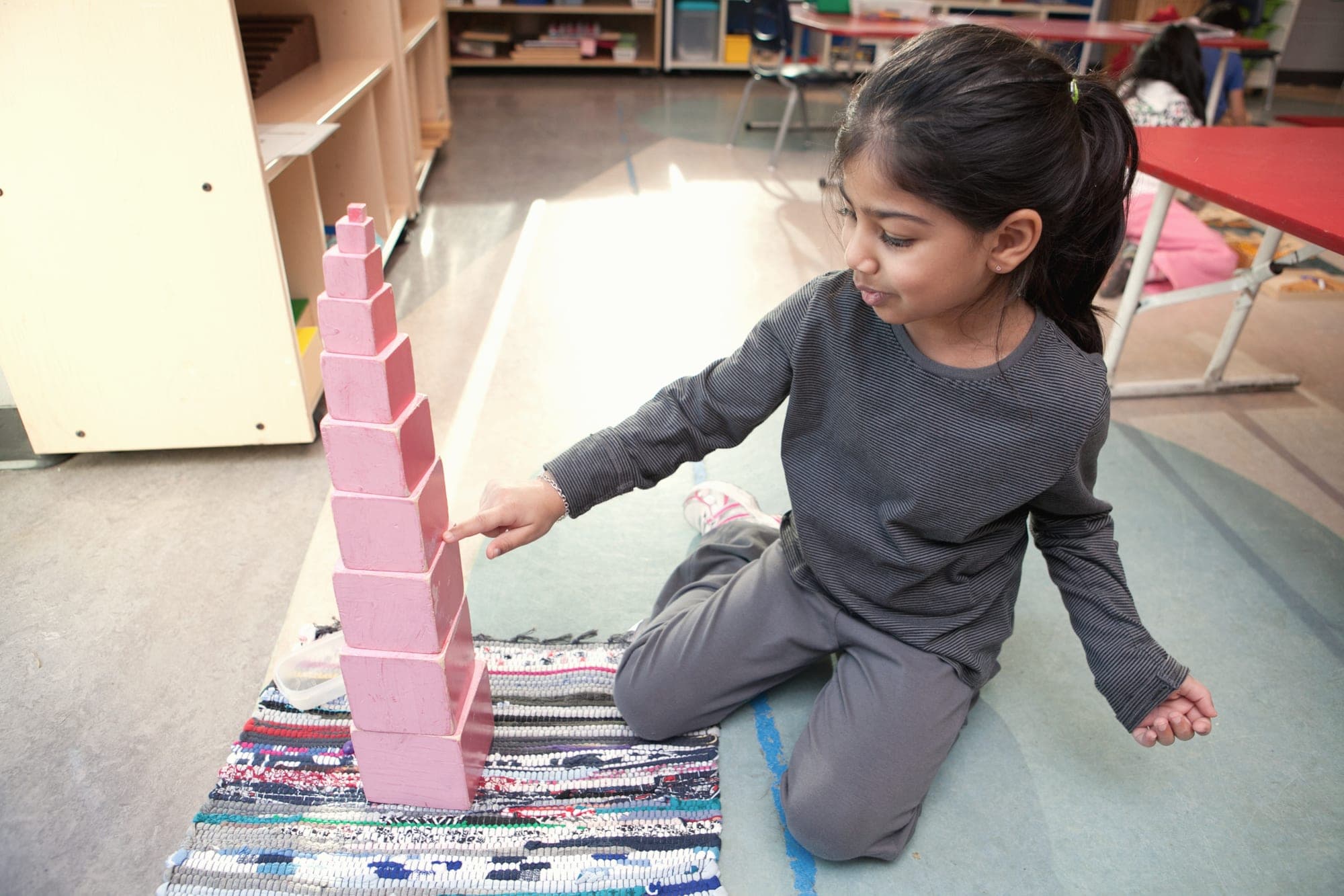 A child pointing at the Montessori pink tower she has built