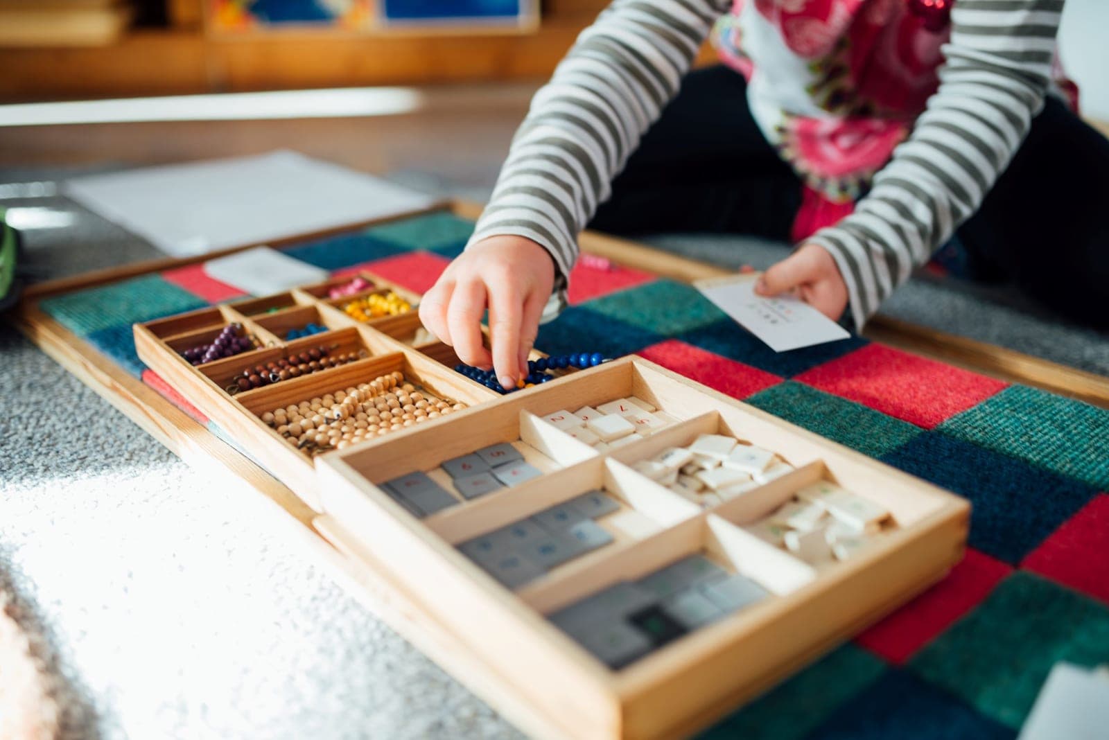A child's hands exploring a wooden Montessori bead box