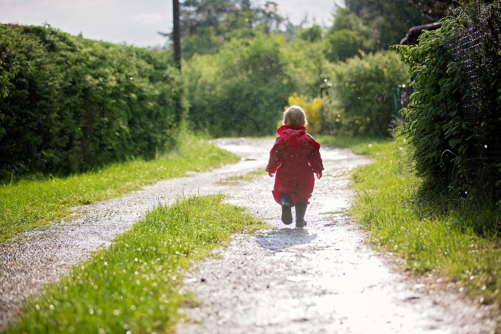 A young child in a red raincoat walking along a green path