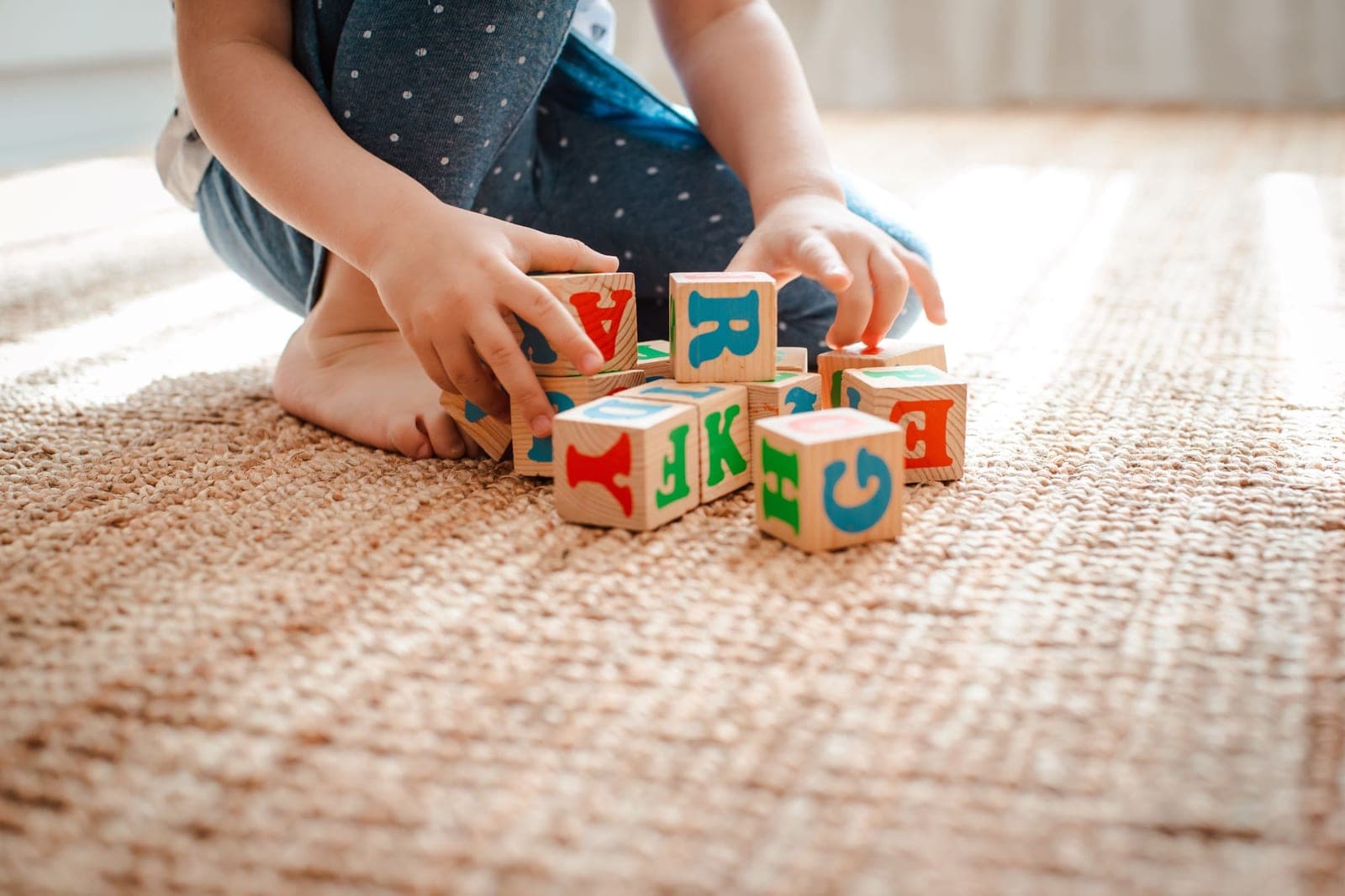 A toddler playing with wooden alphabet blocks on a woven rug