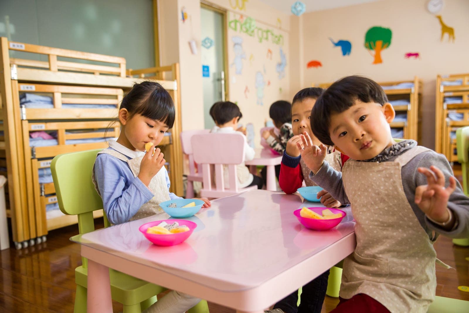 Children at a classroom table eating bowls of fresh fruit at snack time