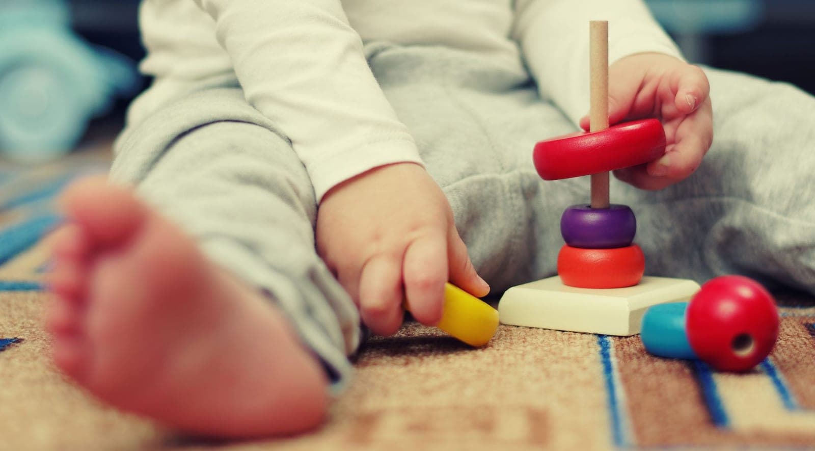 A toddler's hands stacking coloured wooden rings on a peg